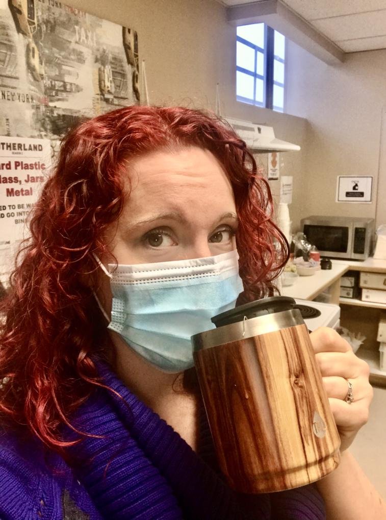 Brienna in a mask with a travel mug at work