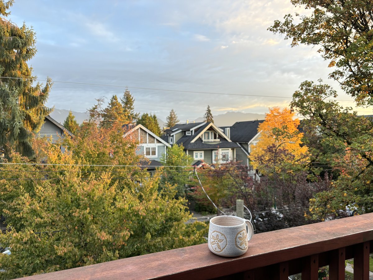 A speckled mug on a balcony rail above autumn trees and the North Shore mountains